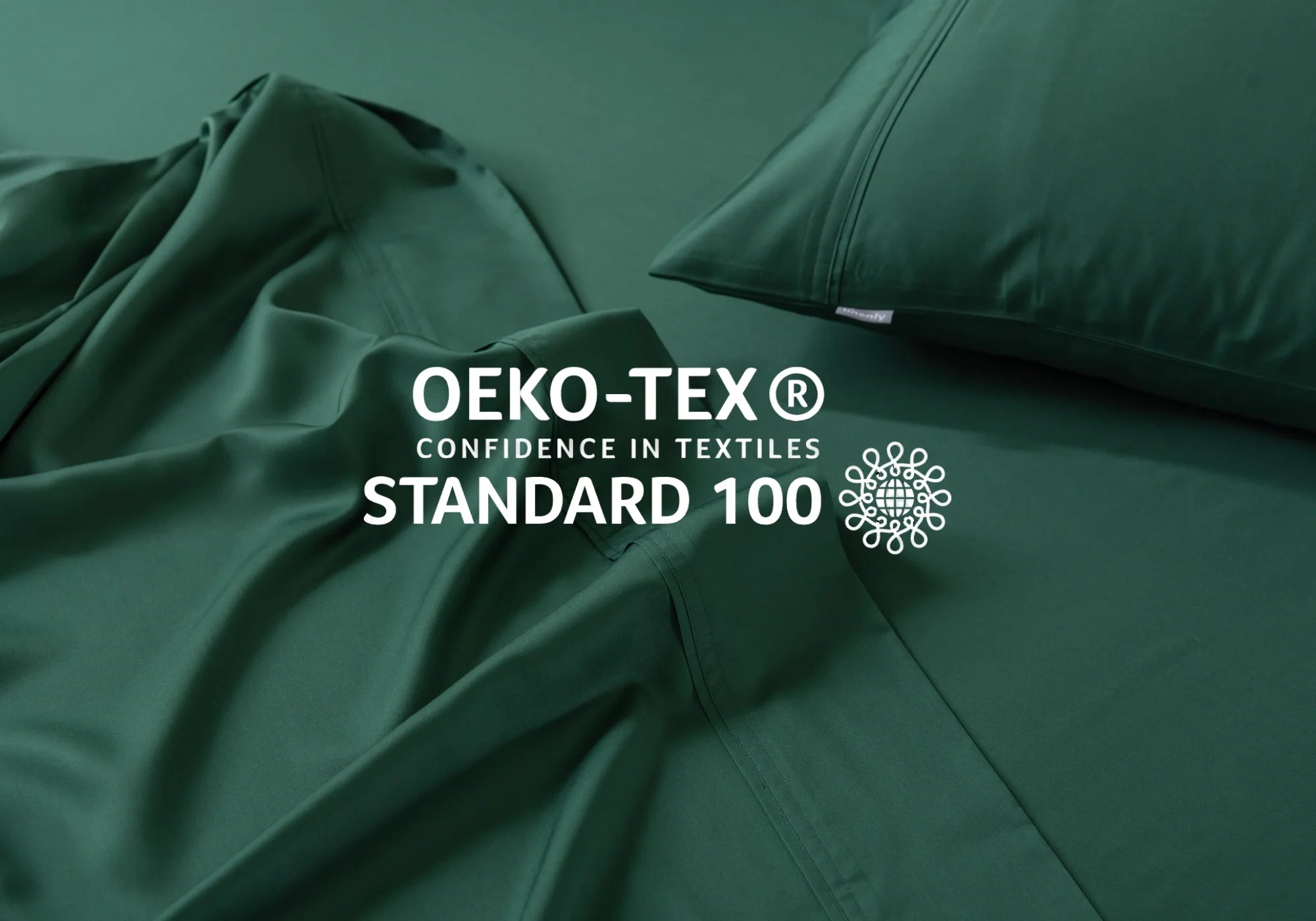 Dark green bed sheets and a pillow are neatly arranged, with the OEKO-TEX® STANDARD 100 certification logo and text “Confidence in Textiles” displayed prominently over the fabric.