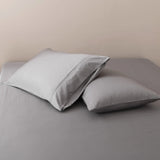 Two plush pillows with Linenly Bamboo Pillowcase Sets in Stone Grey on a neatly made bed with a smooth gray satin weave bedsheet.