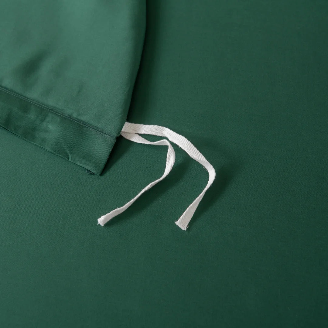 Flat-lay image of a dark green fabric drawstring bag on matching surface, made from premium bamboo materials. The white drawstrings contrast with the deep green background, echoing the essence of Linenly���s Bamboo Quilt Cover - Ever