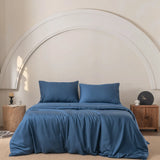 The room features a Linenly Bamboo Quilt Cover in Midnight with a silky texture and two pillows neatly on the bed. Wooden nightstands, each holding a candle and clock, flank the bed. A decorative white arch adorns the wall, with a beige rug on the floor completing the look.