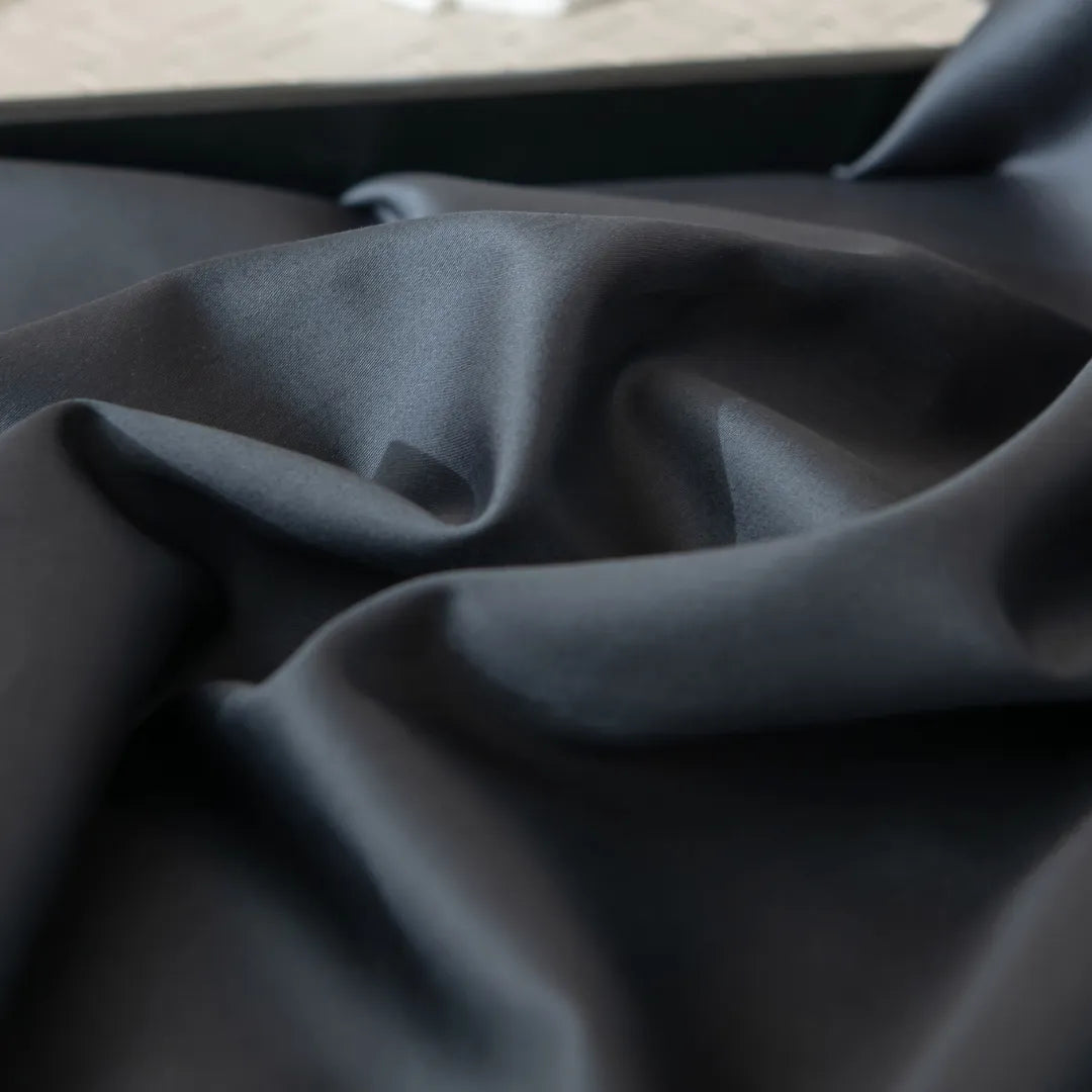 A close-up of the Luxe Cotton Sateen Flat Sheet - Charcoal by Linenly shows smooth black fabric with gentle folds and a soft sheen, highlighting its luxurious, silky sateen texture.