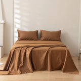 A neatly made bed features the Linenly Luxe Cotton Sateen Sheet Set in terracotta with two matching pillows, set against a light wall and wooden floor in a minimalist room where natural light casts soft shadows.