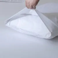 A hand is placing or removing a white pillow into a white pillowcase on a plain, light-colored surface.