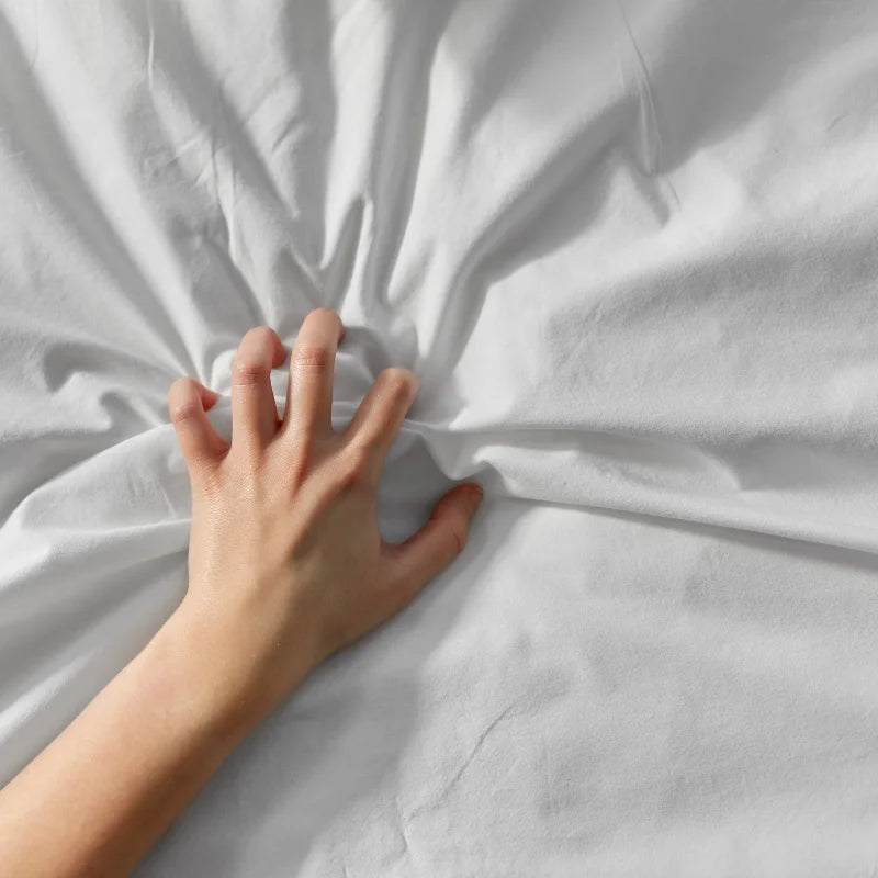 A hand gripping and wrinkling white bed sheets, with fingers spread and pressing into the fabric.