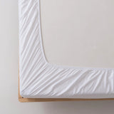 A close-up of a neatly made bed corner with the Linenly Bamboo Fitted Sheet - White, featuring deep sides snugly wrapped around a mattress on a light wooden bed frame.