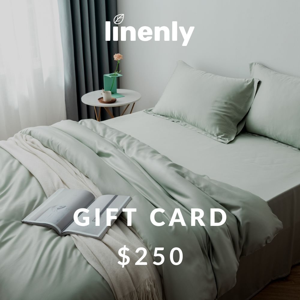 A neatly made bed with light green sheets and pillows is pictured, promising a good night's sleep. An open book lies on top of a light beige blanket draped over the bed. A small bedside table with a potted plant and mug adorns the background. Text reads "Linenly Gift Cards $250".